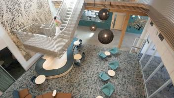 Modern atrium with suspended white spiral staircase, teal lounge chairs, round tables