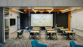 Modern classroom with movable desks, teal lounge chairs, projector screen and whiteboards