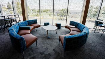 Curved blue-and-tan sofas around round tables by floor-to-ceiling windows overlooking trees.