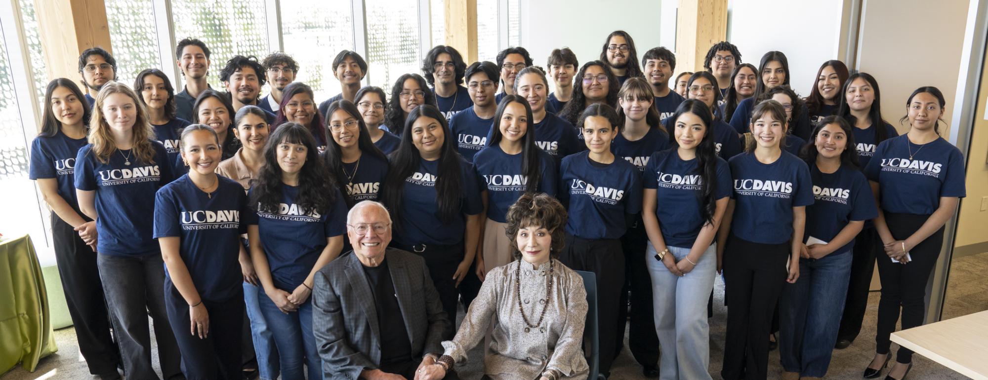 Group photo of diverse women and two seated adults in office, navy shirts, smiling