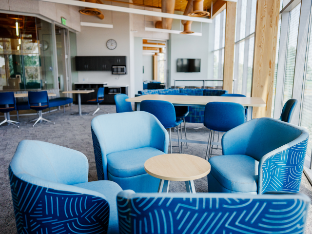 Bright modern lounge with blue curved sofas around round tables by tall windows.