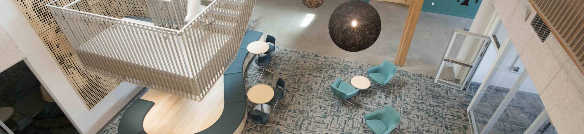Modern atrium with suspended white spiral staircase, teal lounge chairs, round tables
